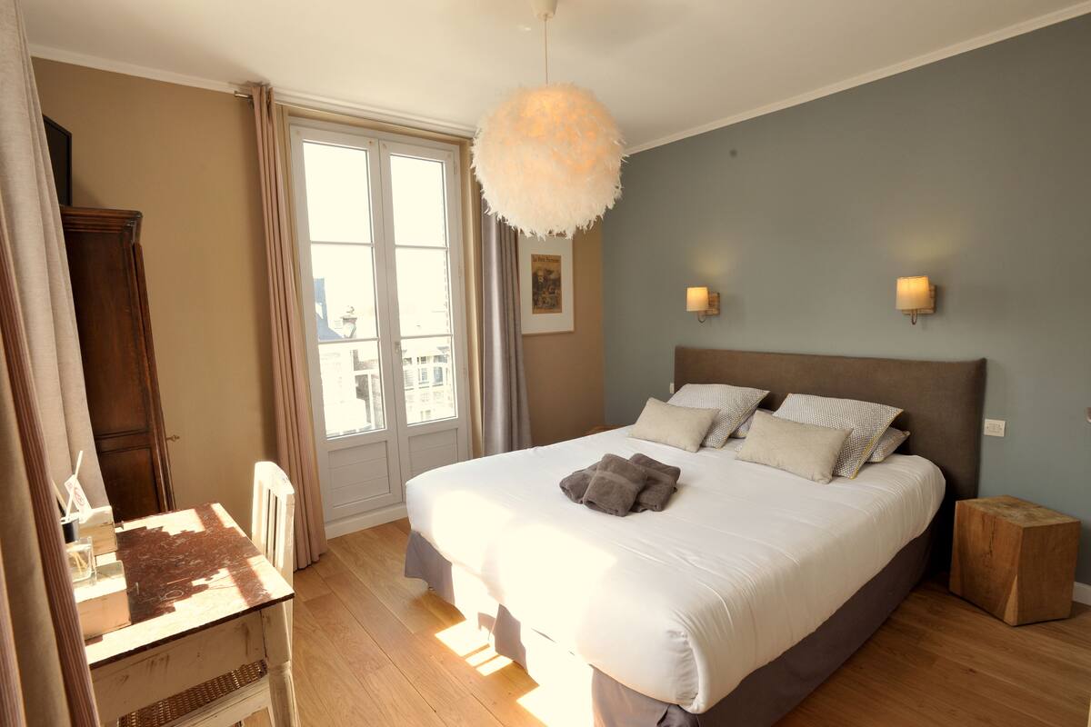 A bedroom with a large bed, a wooden nightstand, a dresser, and a window with curtains.