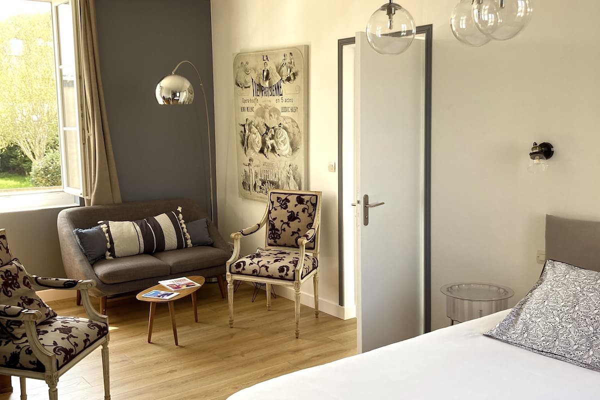 A bedroom with a large bed, a sofa, a chair, a small table, and a wall-mounted light fixture.