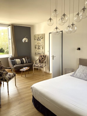 Un dormitorio con una cama grande, un sofá, una silla, una mesita y un aplique de pared.