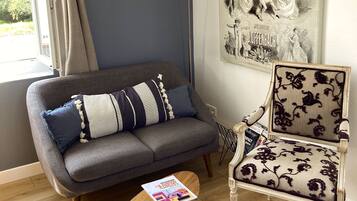 Un salon avec un canapé gris, un fauteuil à motifs, une lampe sur pied et une affiche accrochée au mur.