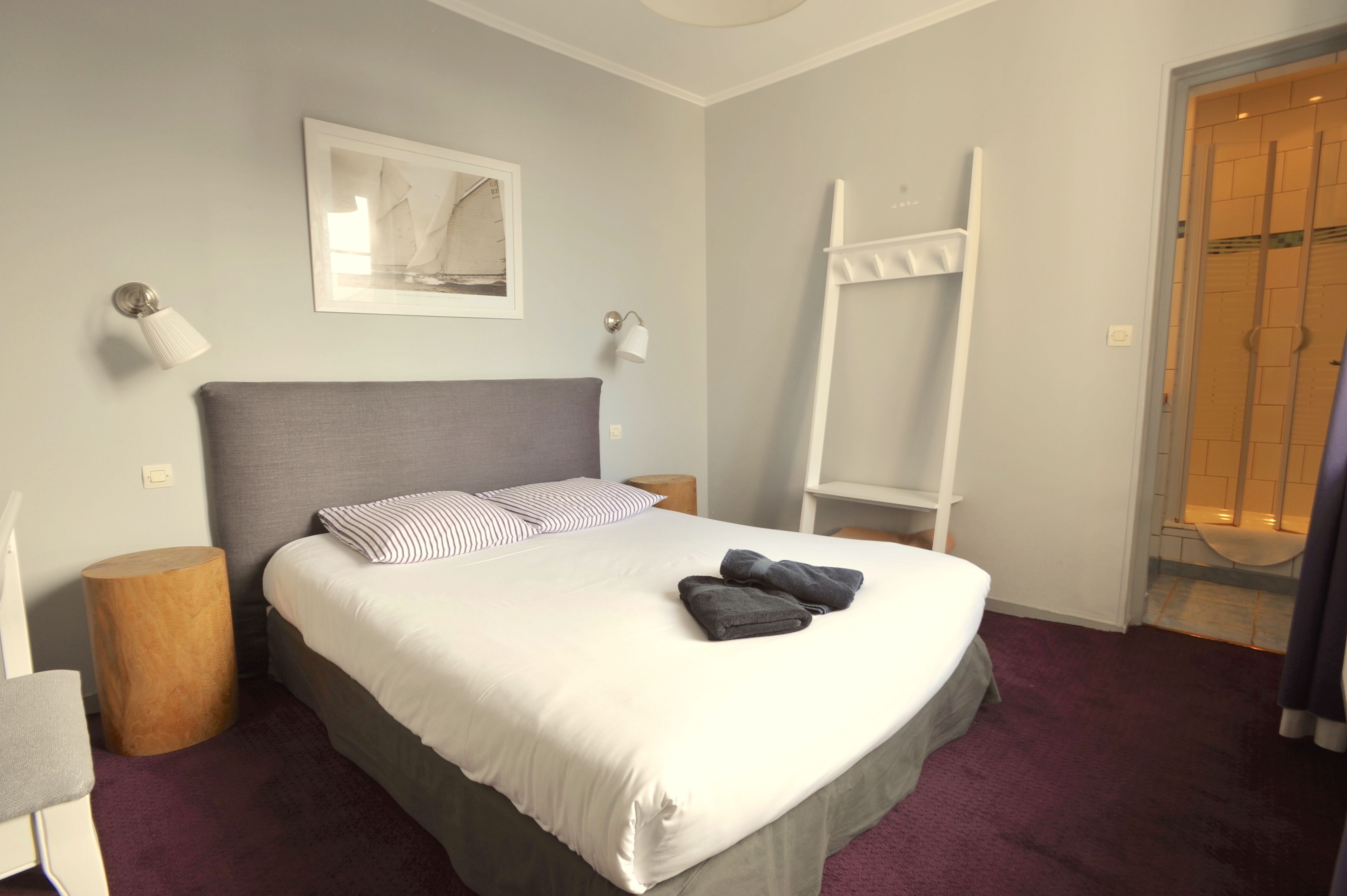 A neatly made bed with pillows, a bedside lamp, a wooden side table, and a towel on the bed.