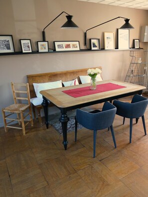 Un comedor con una mesa de madera, sillas azules, un mantel individual rojo y un jarrón con flores blancas.