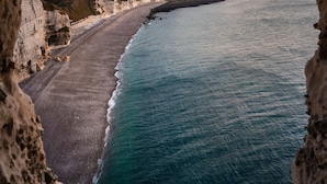 A coastal view through a cave opening, featuring a sandy beach and cliffs. - Hotel d'Angleterre (Etretat)