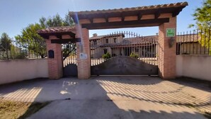 A gated entrance with a brick archway and a metal gate, leading to a building with a tiled roof. - La Contrada (Arens de Lledo)