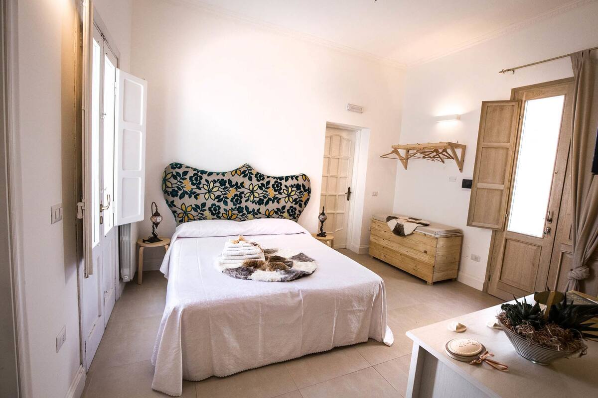 A bedroom with a bed, bedside table, dresser, and a window.