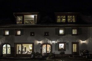 Un edificio de dos pisos con una entrada bien iluminada, ventanas grandes y un segundo piso visible con un balcón.