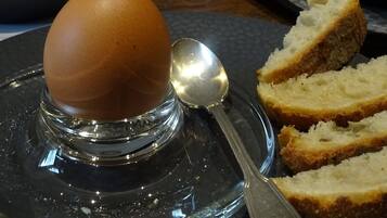 A clear glass plate with a single egg on a stand, accompanied by a spoon and slices of bread.