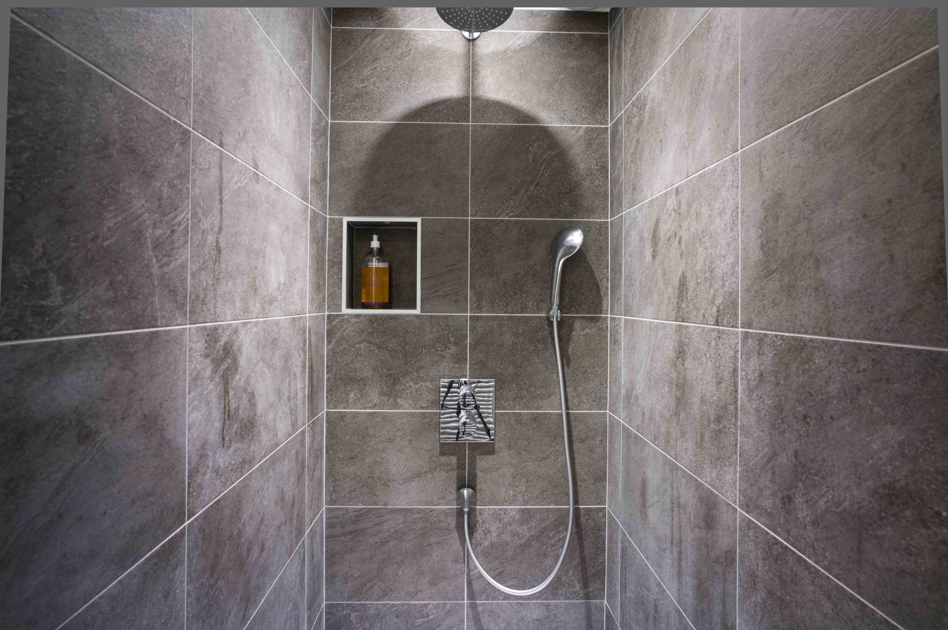 Un espace douche moderne doté d’un pommeau de douche à main et d’un panneau de commande fixé au mur.