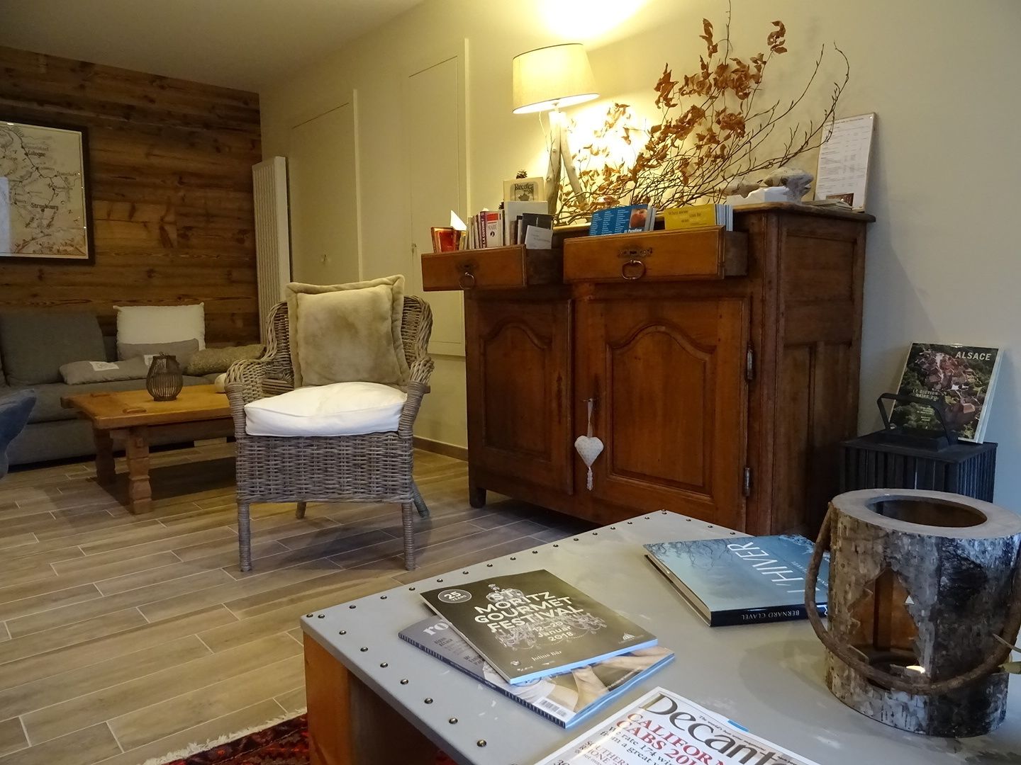 A cozy living room with a wicker chair, a wooden cabinet, and a table with magazines.