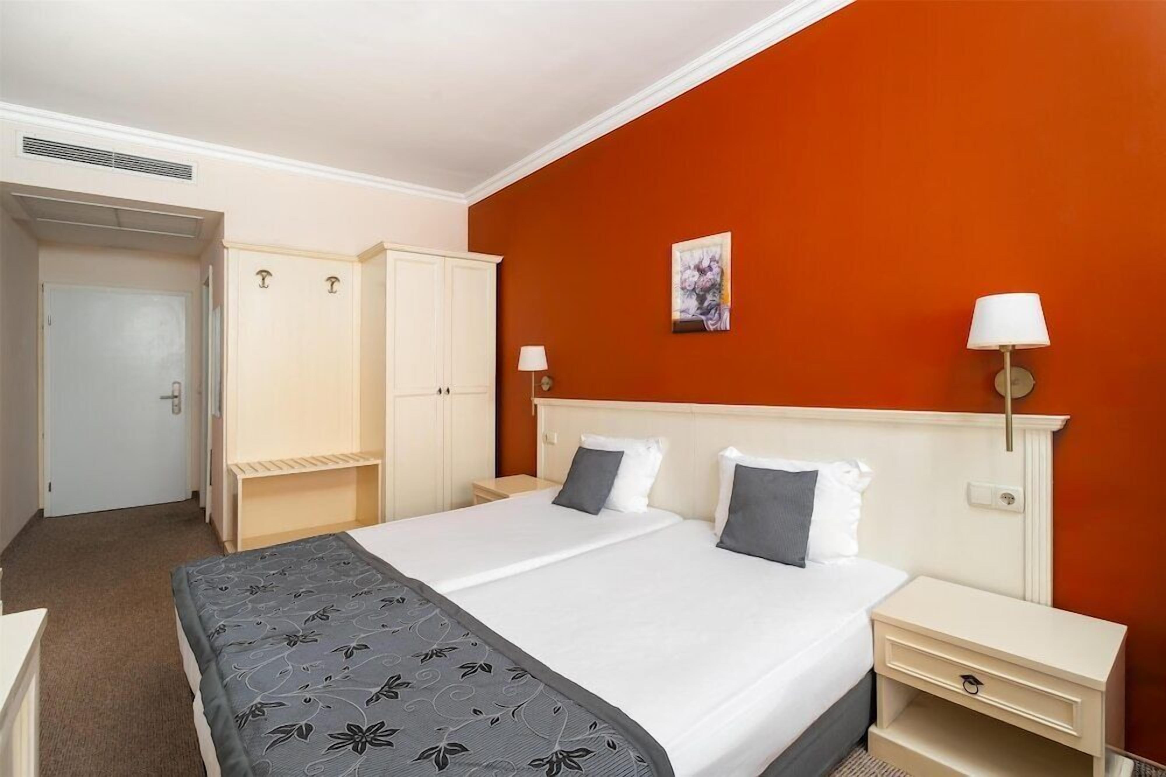 A hotel room with a bed, two bedside tables, a wardrobe, and a painting on the wall.