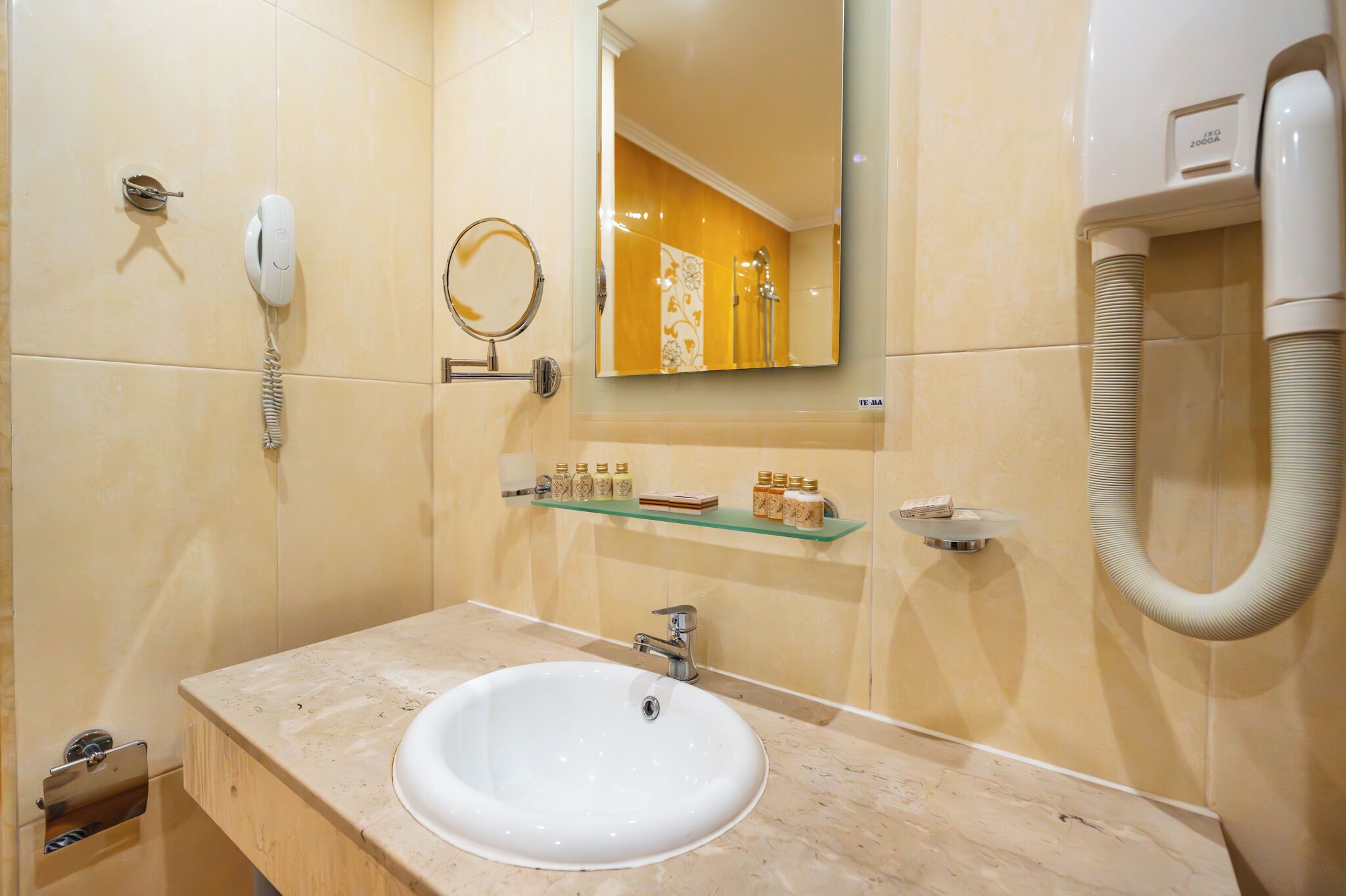 A bathroom with a white sink, a mirror, a telephone, and a shelf with toiletries.