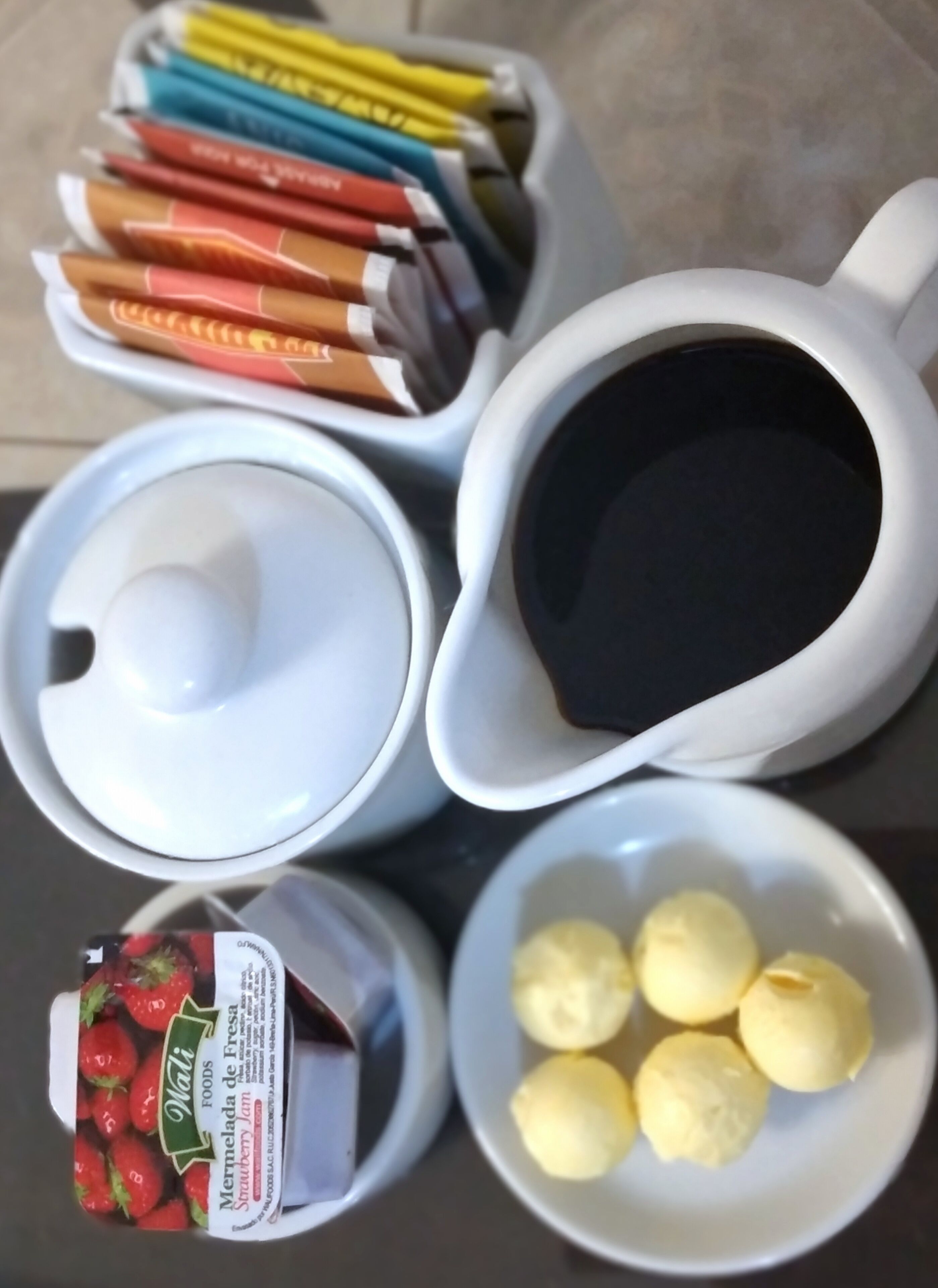 A table with a coffee maker, a jar of strawberry jam, and a bowl of lemons.