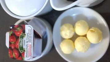 A table with a coffee maker, a jar of strawberry jam, and a bowl of lemons.