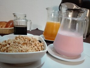 Ein Frühstückstisch mit einer Schüssel Müsli, einer Karaffe rosa Flüssigkeit und einem Glas Orangensaft.