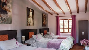 Une chambre d’hôtel avec trois lits, des poutres en bois au plafond et des œuvres d’art accrochées aux murs.
