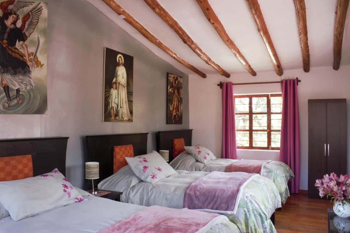 A hotel room with three beds, wooden beams on the ceiling, and artwork on the walls.