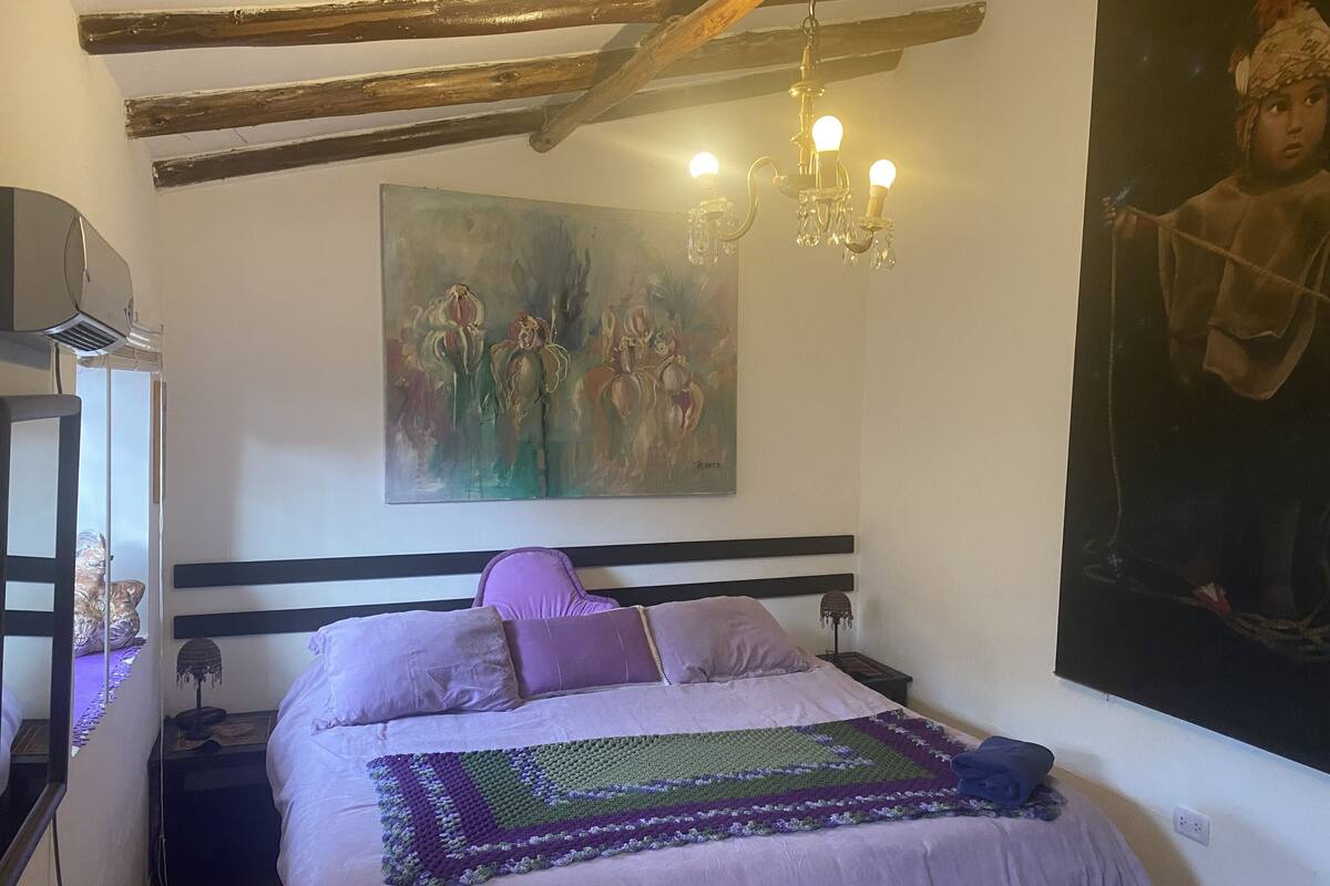 A bedroom with a bed, a painting, a chandelier, and a large artwork on the wall.