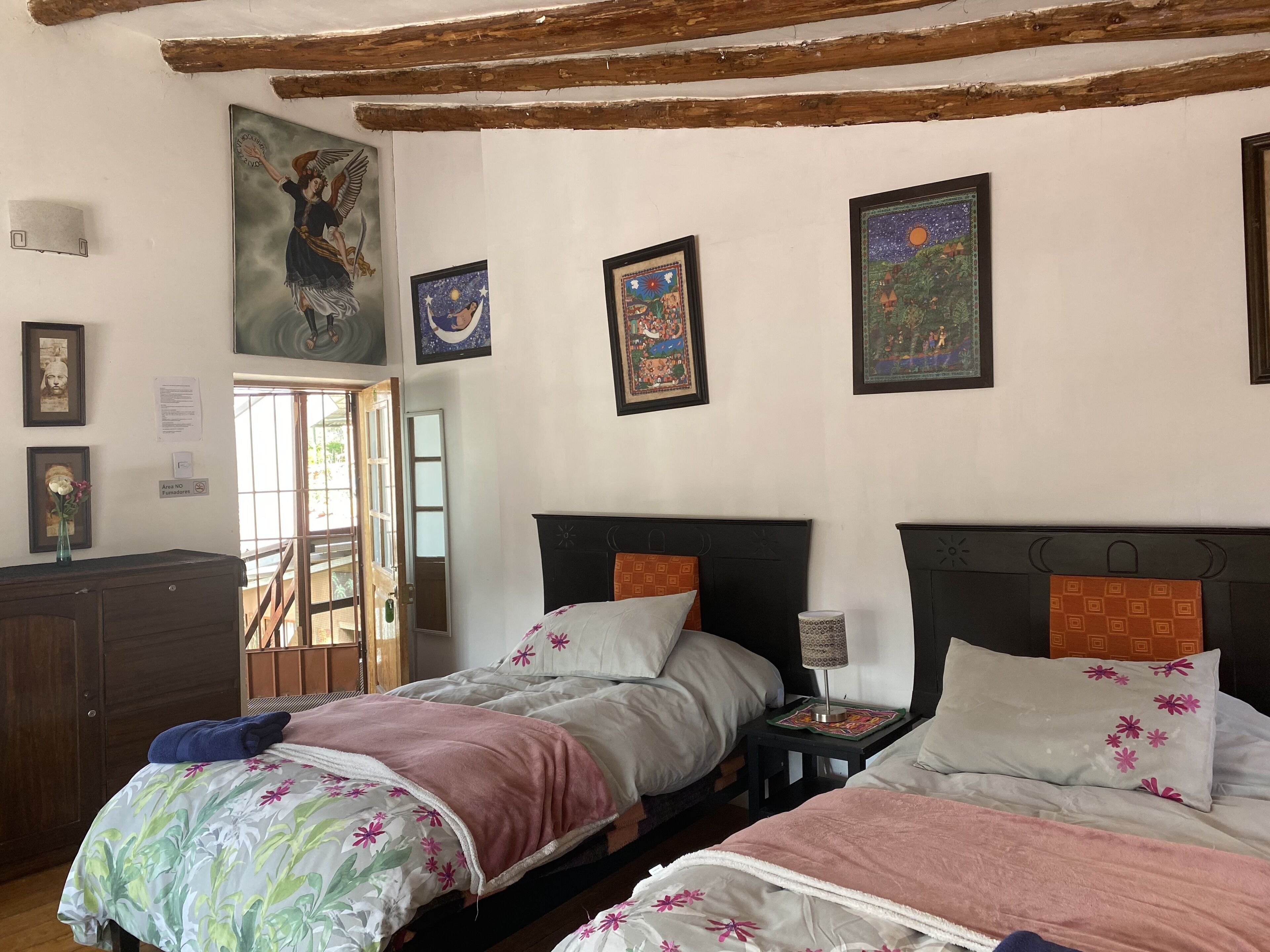 A room with two beds, a wooden headboard, a nightstand with a lamp, and artwork on the walls.