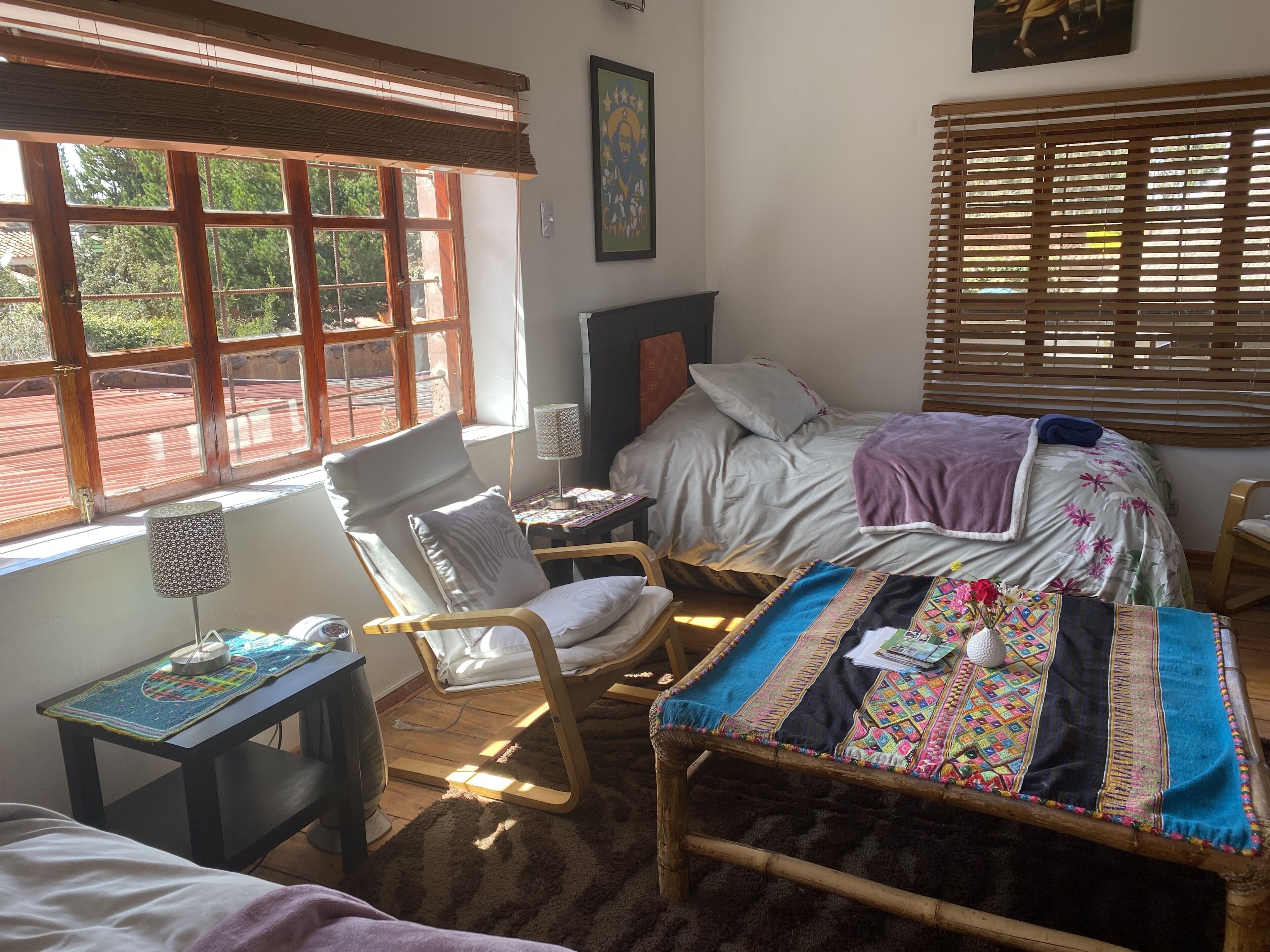 A cozy bedroom with a bed, a chair, a small table, and a window with blinds.