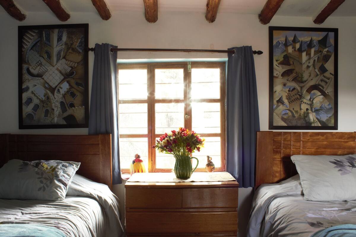 A bedroom with two beds, a wooden dresser, a vase with flowers, and two paintings on the walls.