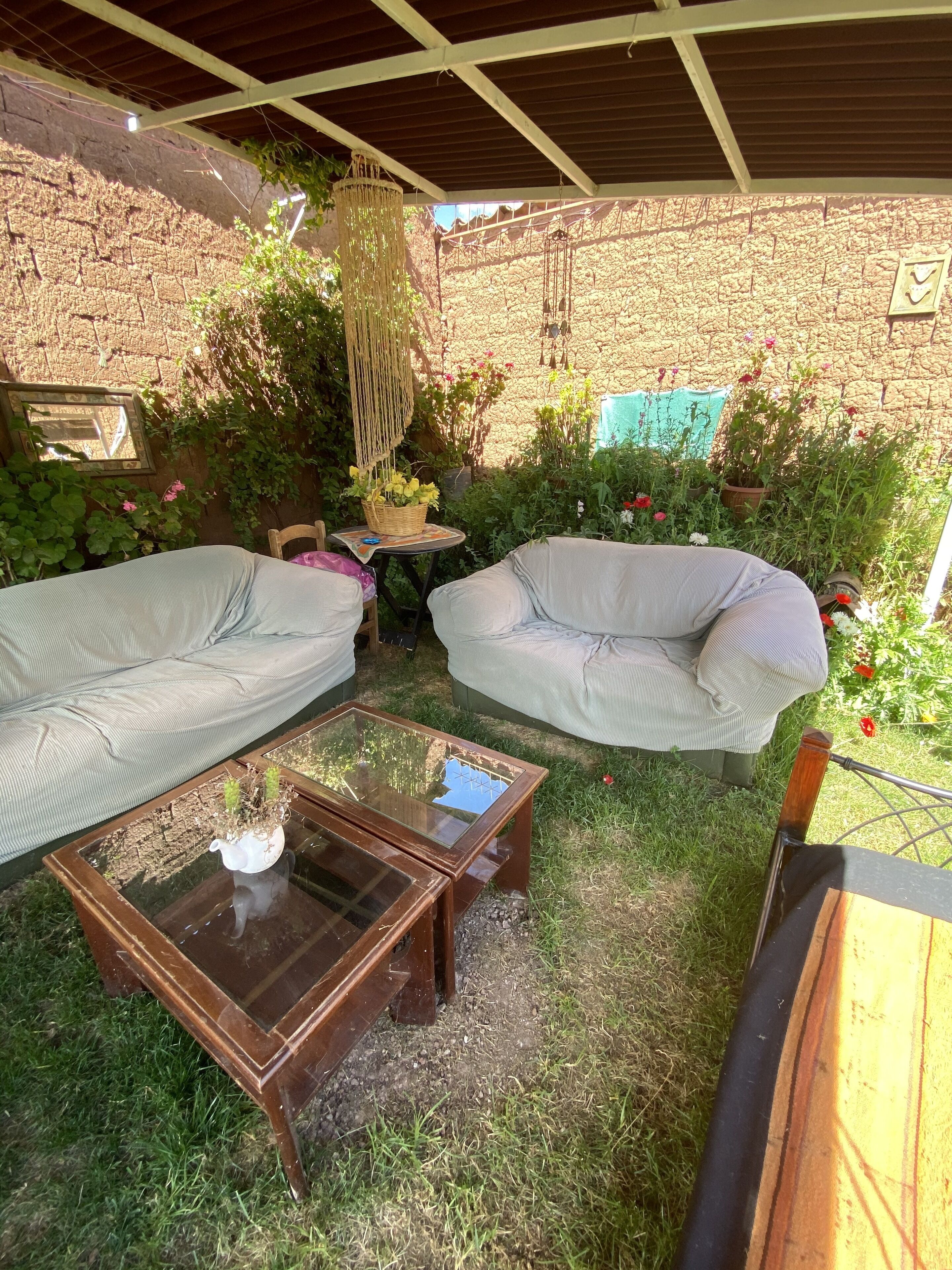 An outdoor seating area with two cushioned sofas, a glass-top coffee table, and a wicker basket with flowers.
