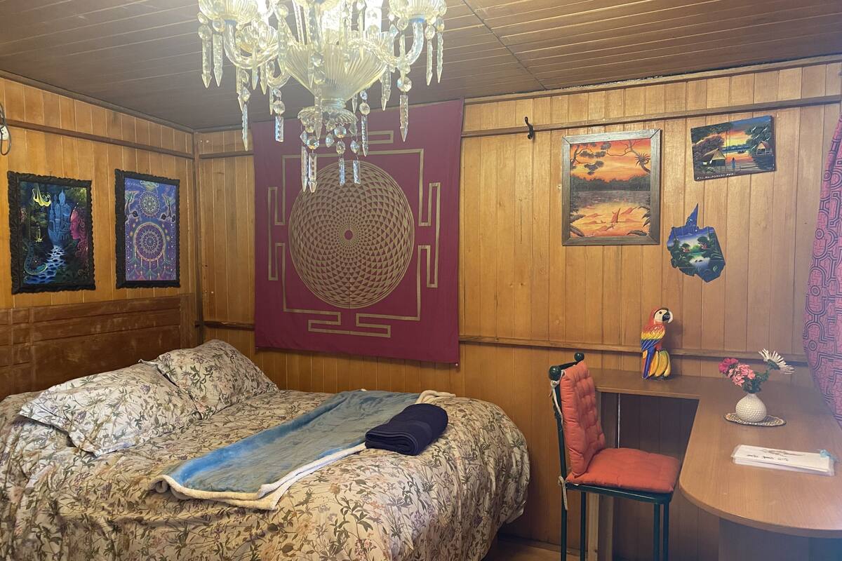 A bedroom with a floral bedspread, a chandelier, wooden walls, and artwork.