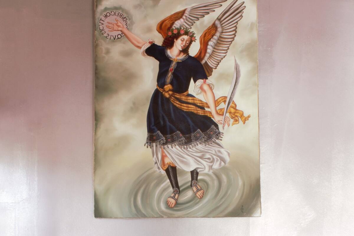 A bedroom with a bed, a pillow, a nightstand, and a wall-mounted painting of an angel.
