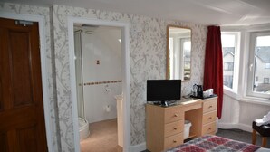 A bedroom with a bed, a desk with a computer, a shower, and a window with a view of buildings. - The Gables (Bathgate)