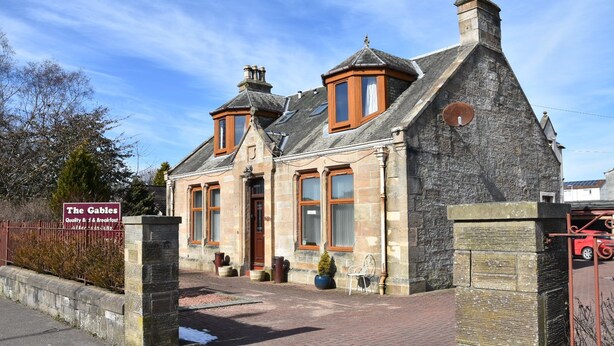 A stone building with a traditional architectural style, featuring a prominent entrance, large windows, and a small turret. - The Gables (Bathgate)