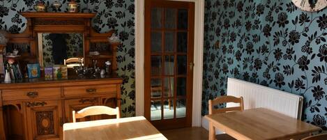 A dining area with a wooden table and chairs, a wooden cabinet with various items, and a door with a glass panel.