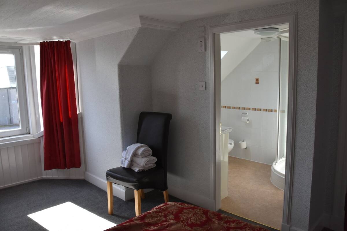 A small, compact room with a black chair, a red curtain, and a glass door leading to a bathroom.