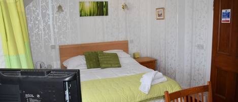 A hotel room with a bed, a desk with a computer, a chair, a door, and a window with curtains.
