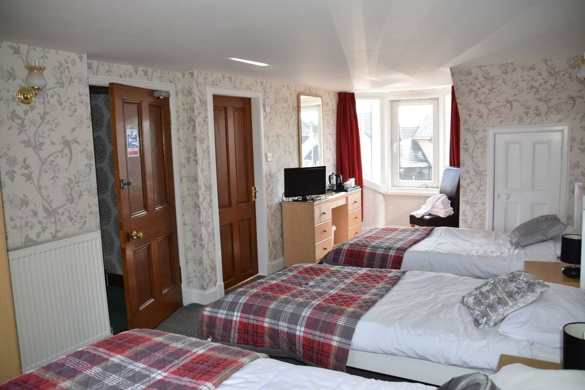 A bedroom with two beds, a dresser, a television, and a window with curtains.