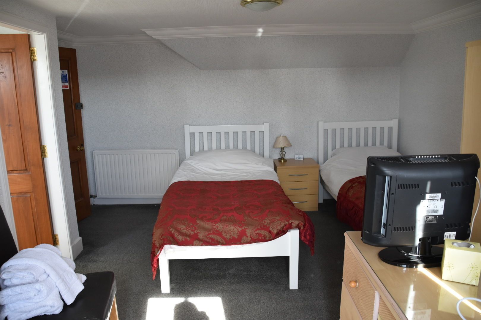 A hotel room with two single beds, a wooden dresser, a television, and a radiator.