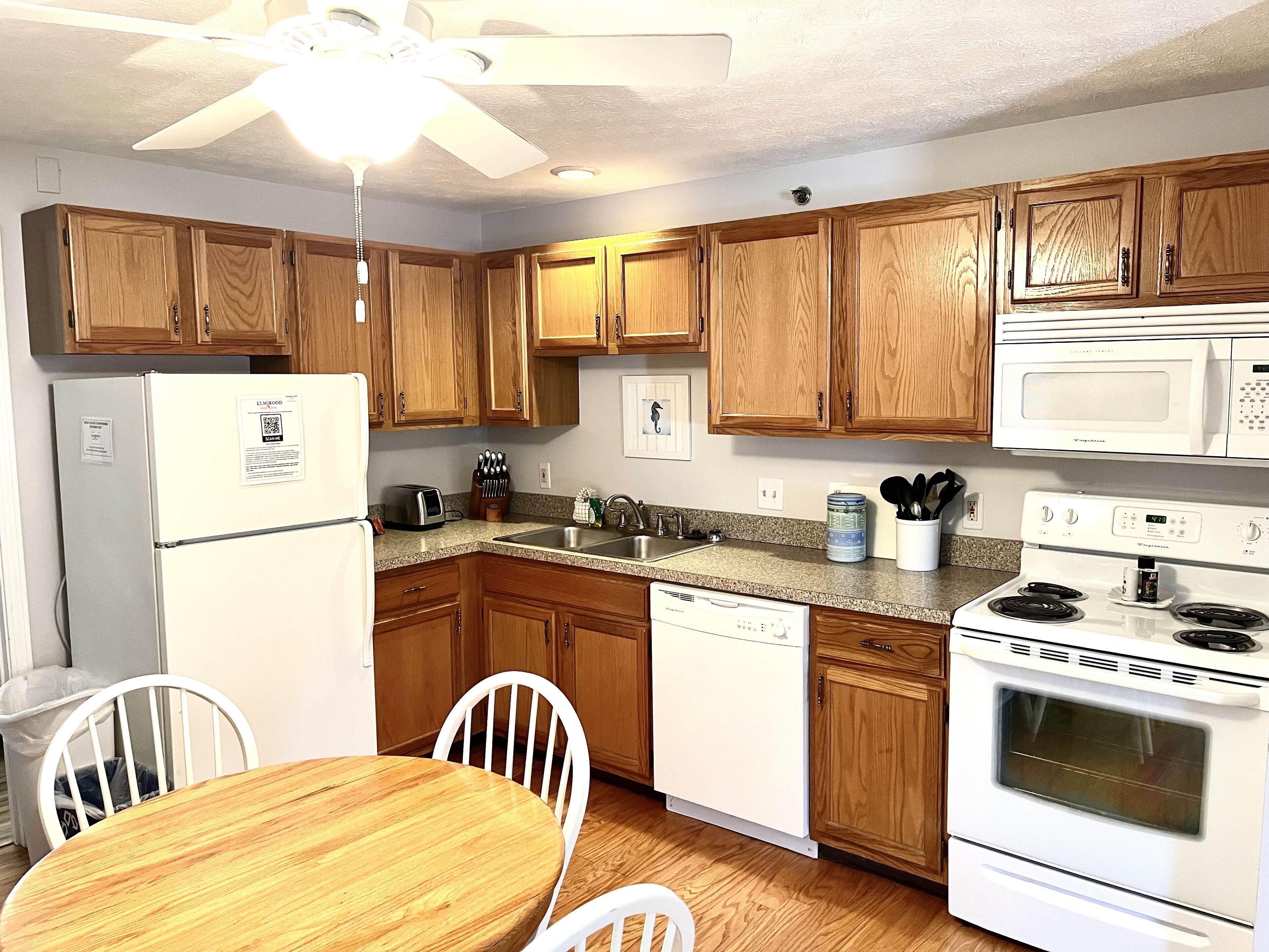 A compact kitchen with wooden cabinets, a white refrigerator, a microwave, a stove, and a dishwasher.