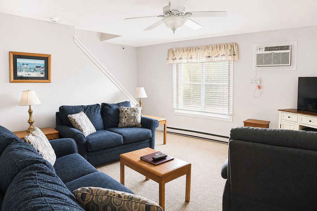 A living room with a sofa, armchair, coffee table, and a ceiling fan.