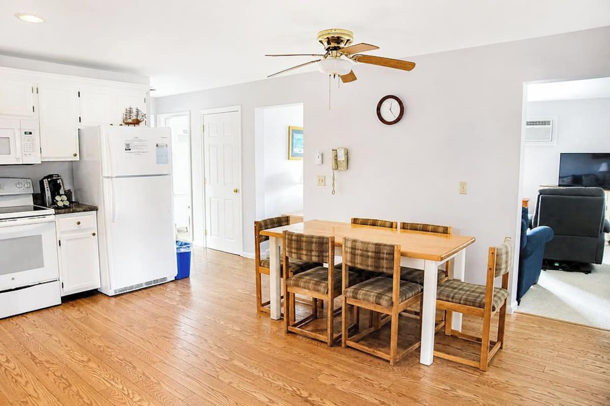 A modern kitchen with white appliances, a dining table with plaid chairs, and a ceiling fan.
