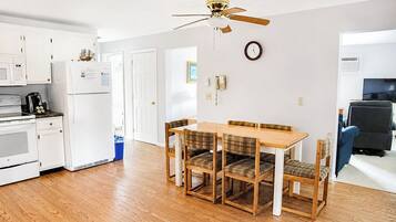 A modern kitchen with white appliances, a dining table with plaid chairs, and a ceiling fan.