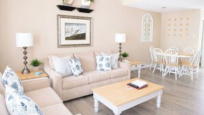 A living room with a sofa, coffee table, and dining area with chairs. - Elmwood Resort Hotel (Wells)