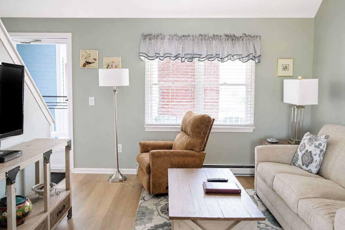 A living room with a sofa, armchair, TV, and a window with blinds.