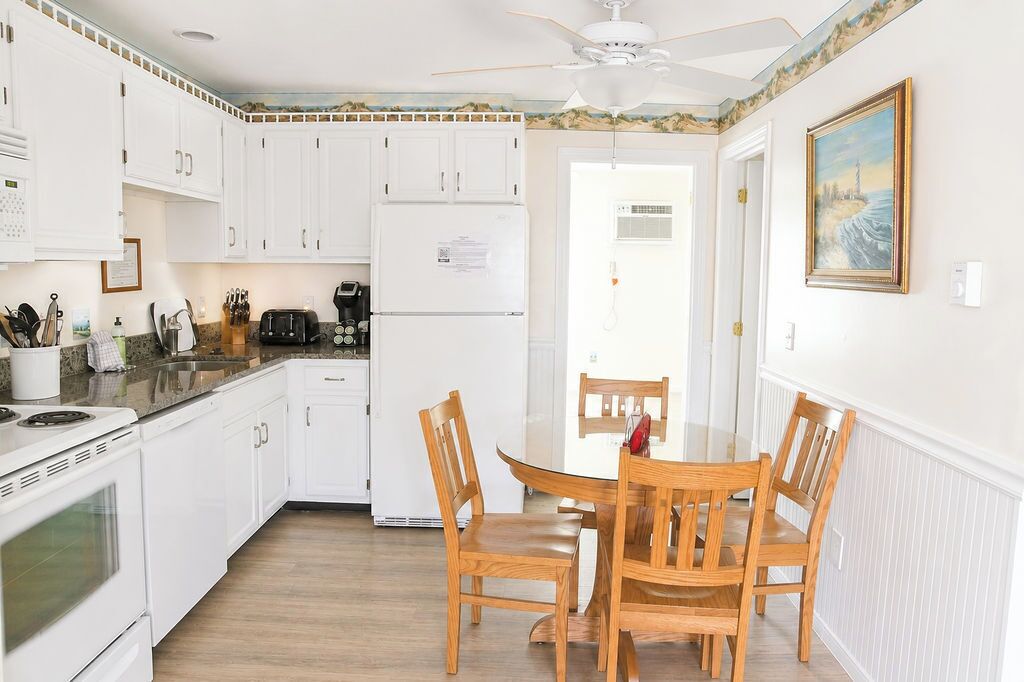 A kitchen with white cabinets, a refrigerator, a stove, and a dining table with chairs.