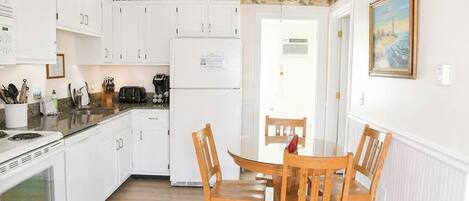 A kitchen with white cabinets, a refrigerator, a stove, and a dining table with chairs.