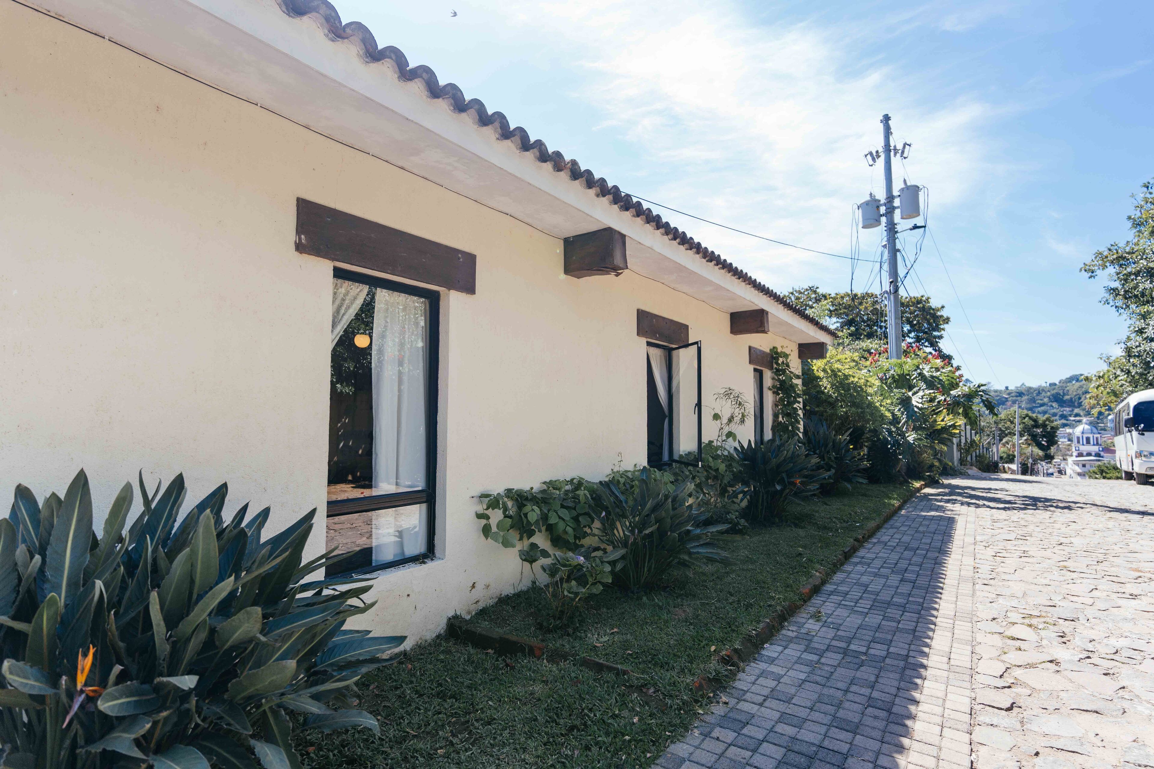 A building with a tiled roof, windows with curtains, and a paved pathway.