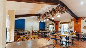 Un vaste espace dédié à la salle à manger, avec de nombreuses tables et chaises, des poutres en bois au plafond et un luminaire décoratif suspendu.