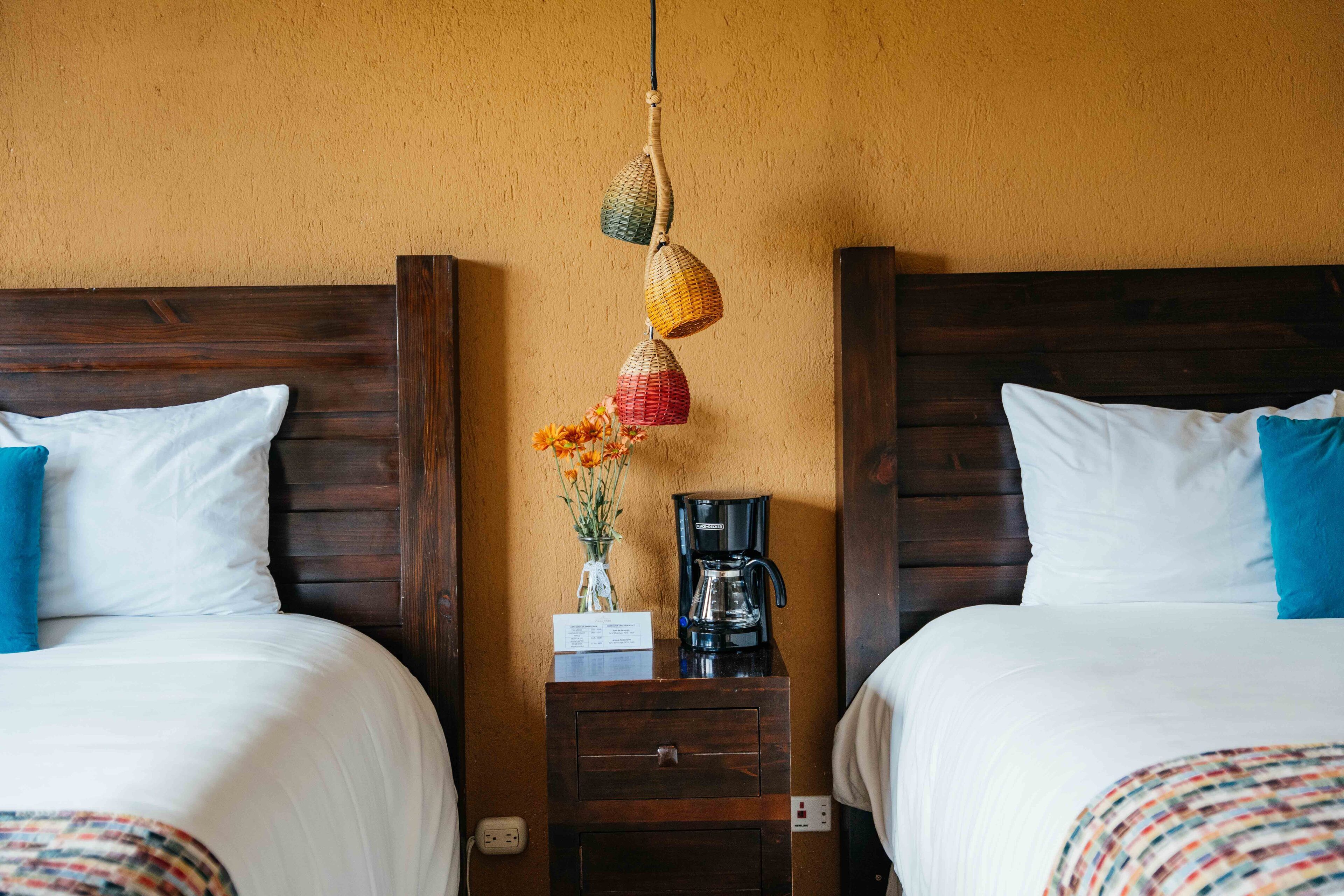 A hotel room with two beds, a nightstand with a coffee maker, and a vase with flowers.