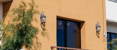 A building with a flat roof, a balcony with a metal railing, and two wall-mounted lanterns.