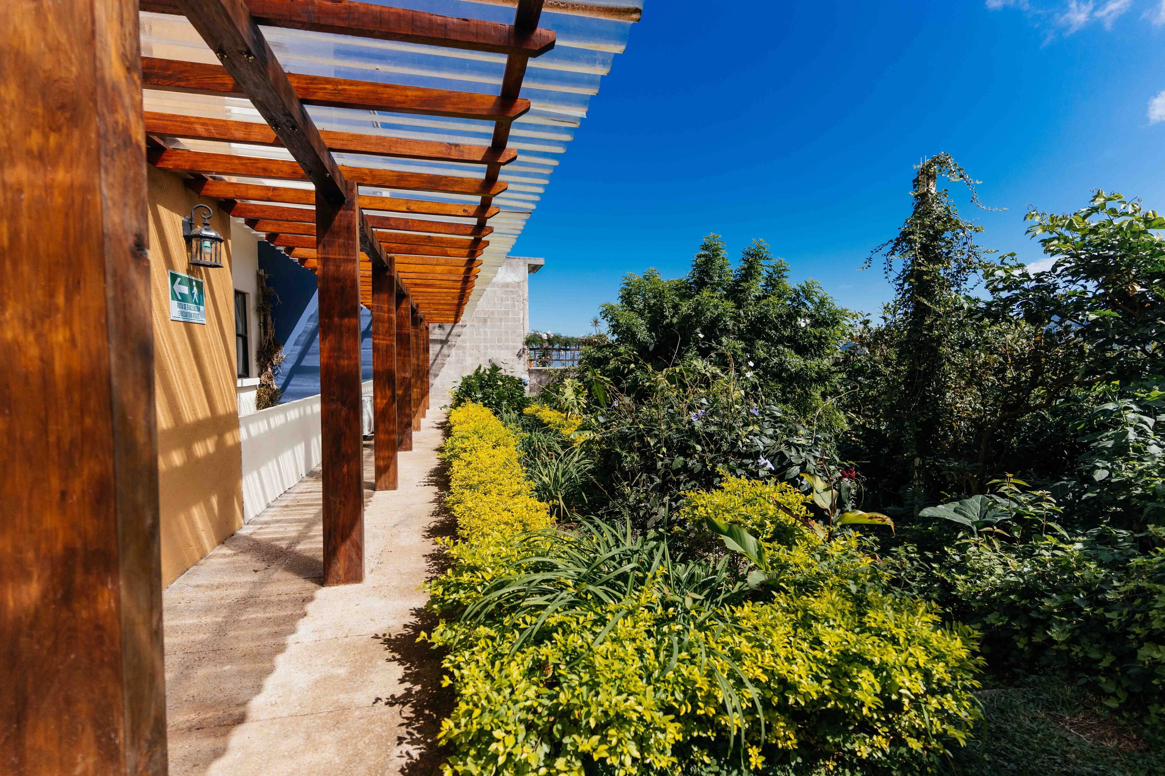A covered outdoor area with wooden beams and a concrete path leading to a building entrance.