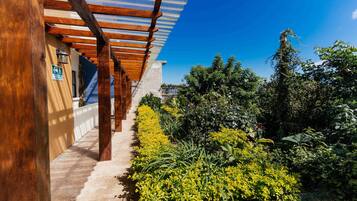 A covered outdoor area with wooden beams and a concrete path leading to a building entrance.