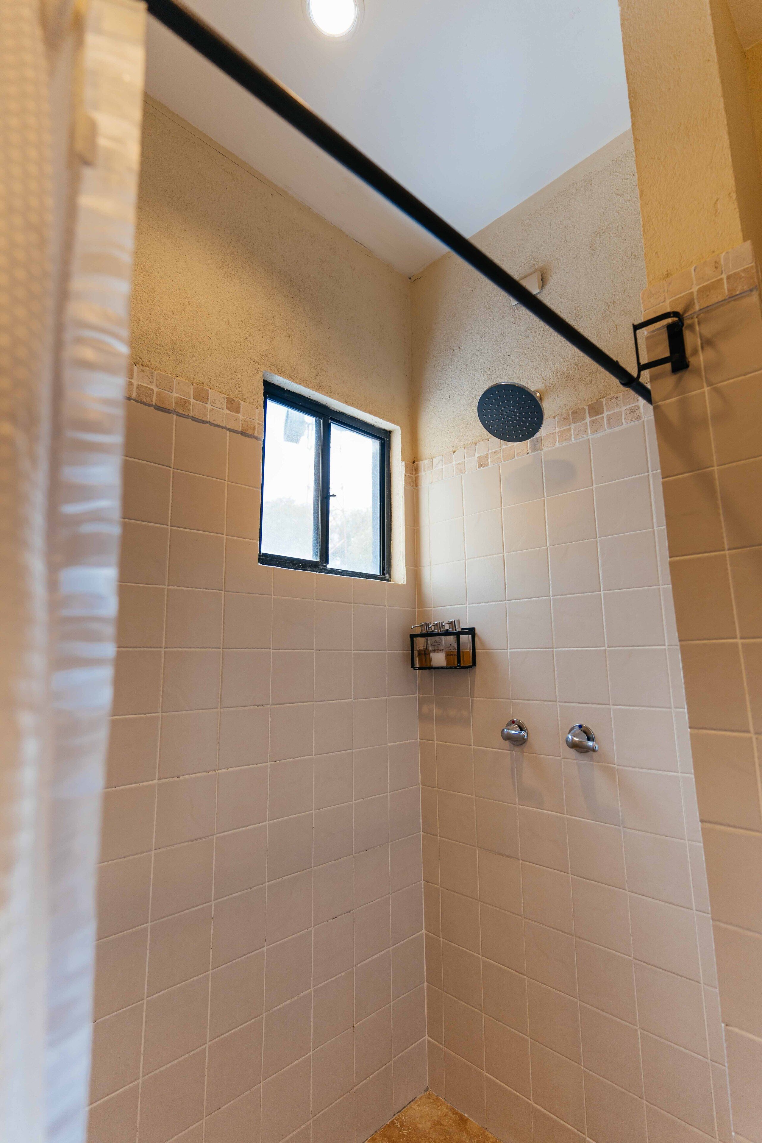 Un espace douche avec des carreaux de couleur beige, une fenêtre et une pomme de douche en métal.