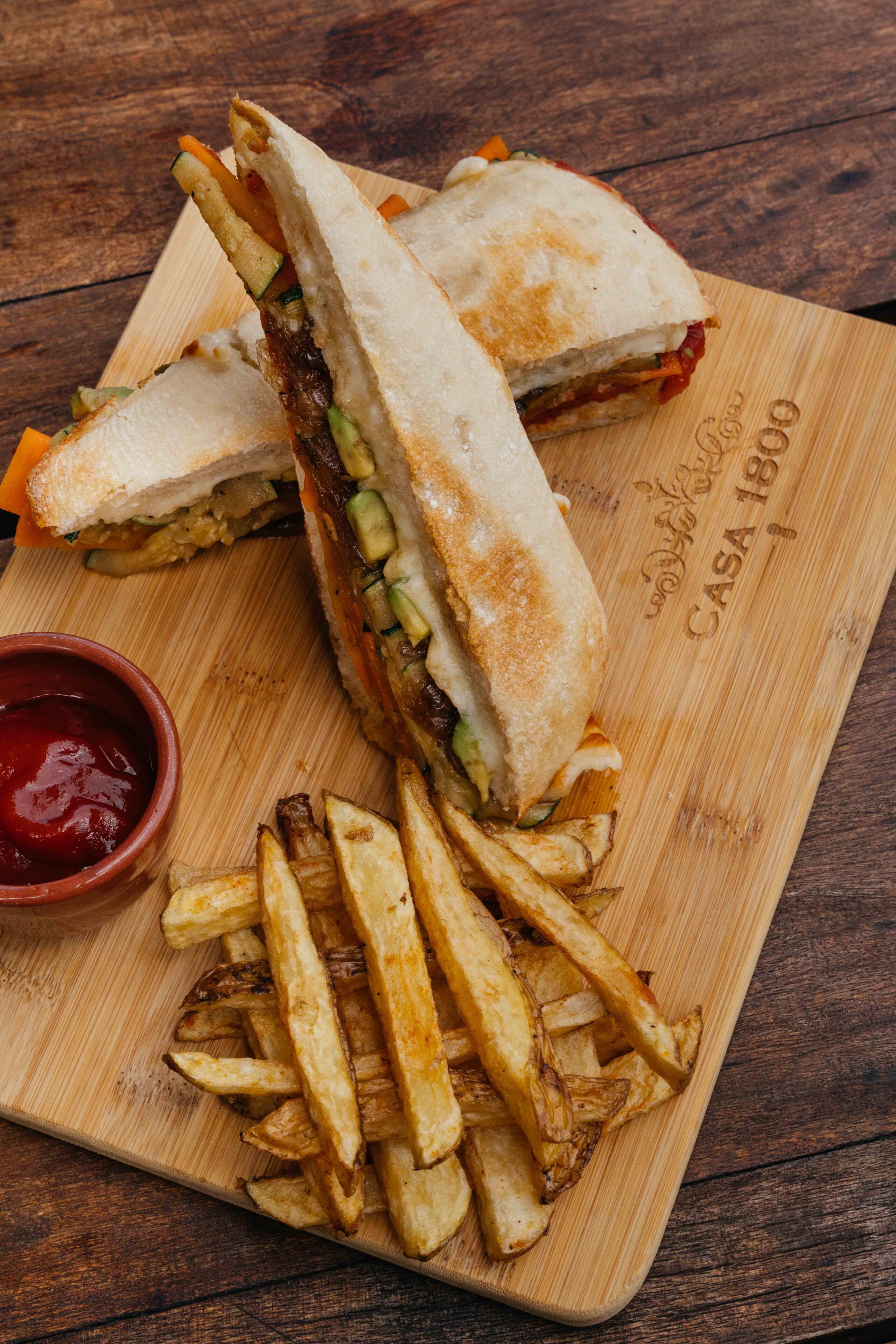 A sandwich cut in half on a wooden board with fries and ketchup.